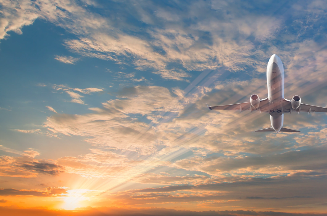 A picture of a white passenger plane from below, against a blue sky filled with clouds and a lens flare from the sun A picture of a white passenger plane from below, against a blue sky filled with clouds and a lens flare from the sun
