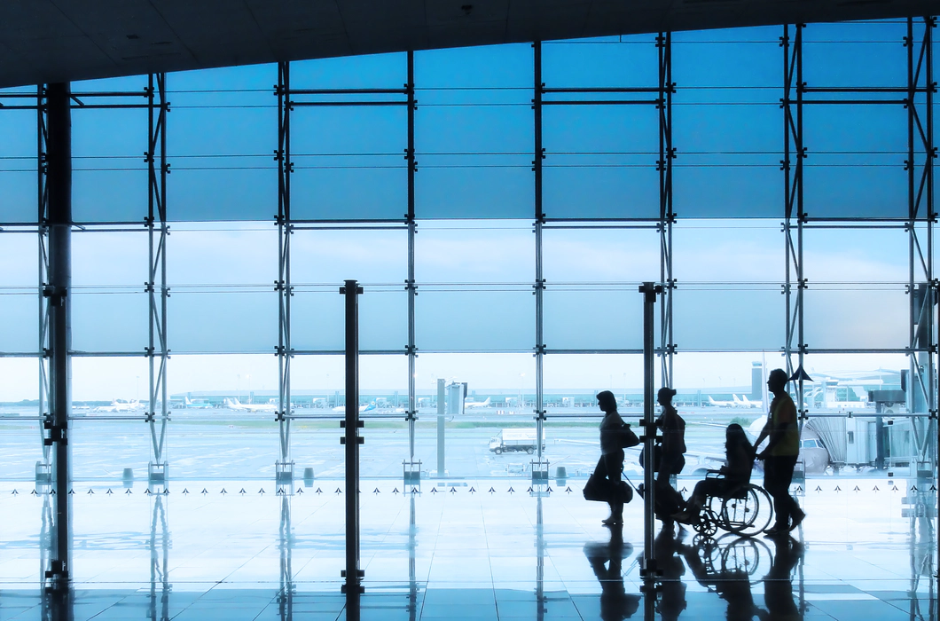 Four silhouettes of people in an airport setting, with a man and woman walking together with suitcases, followed by a wheelchair user being pushed by another person Four silhouettes of people in an airport setting, with a man and woman walking together with suitcases, followed by a wheelchair user being pushed by another person